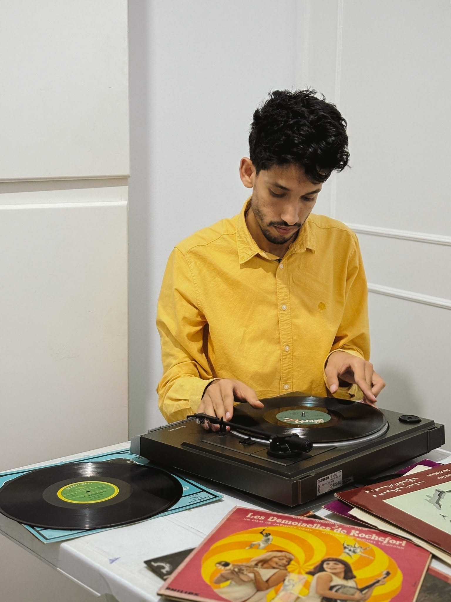 Person in a yellow shirt at a vinyl turntable surrounded by records