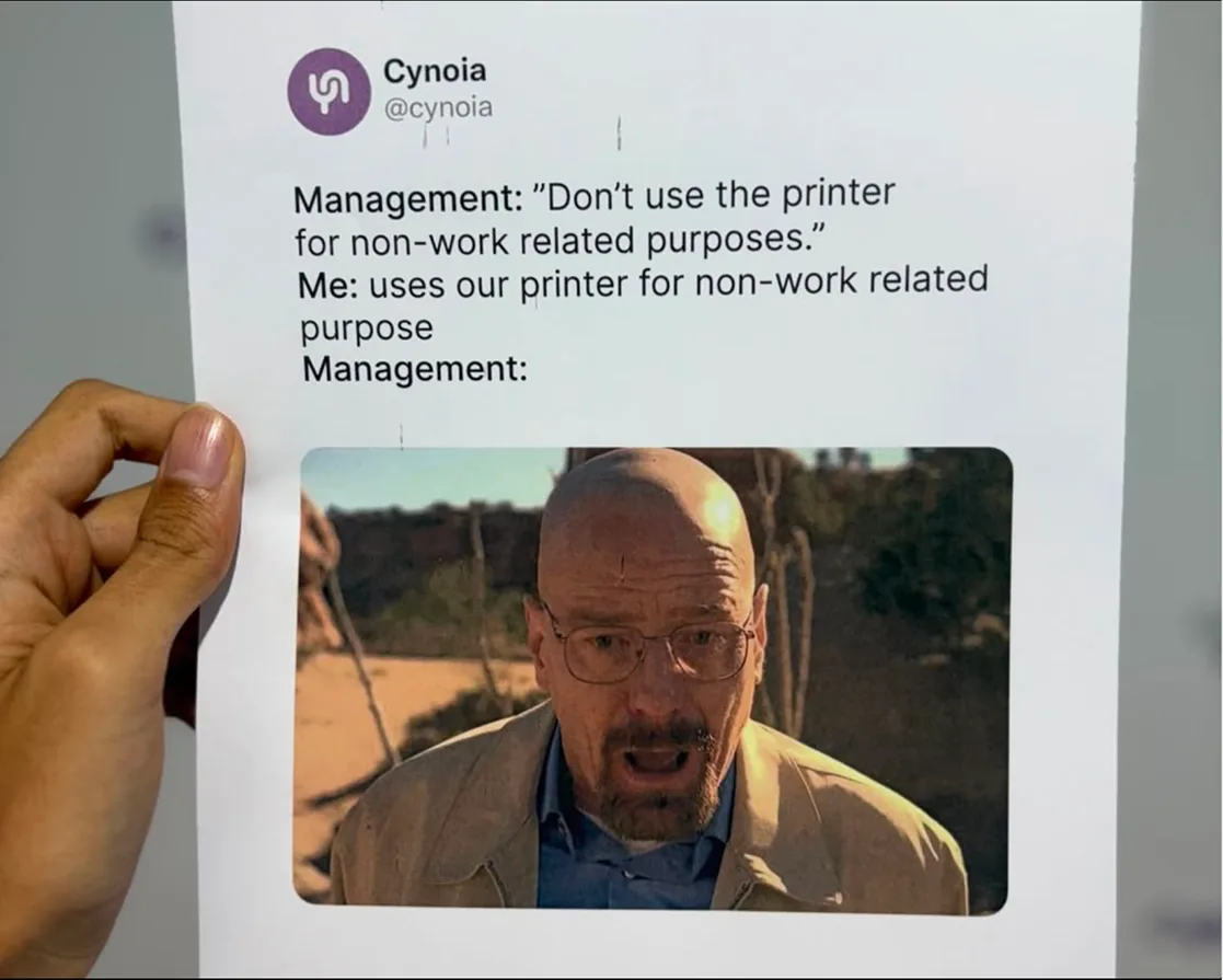 Cynoia meme: a printed tweet held up to the camera joking about using the office printer for non-work purposes, over a stunned reaction photo